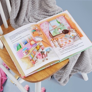 Pode incluir: Um livro infantil aberto com ilustra&ccedil;&otilde;es coloridas. O texto diz: "Era a noite anterior ao dia 7 de agosto. Amanh&atilde; era o anivers&aacute;rio da Matilda. Enquanto o sol se punha no c&eacute;u, ela sussurrou: 'De onde v&ecirc;m as surpresas de anivers&aacute;rio?' Toc, toc, arranha, arranha. Um par de asas bateu perto da janela. 'Ol&aacute;', disse Amelia, 'quem &eacute; voc&ecirc;?' 'Eu sou Griffin, o porquinho da &iacute;ndia do anivers&aacute;rio', guinchou uma pequena criatura. 'Tr&ecirc;s amanh&atilde;!' ele gritou. Griffin sabia a idade de todas as crian&ccedil;as do mundo."