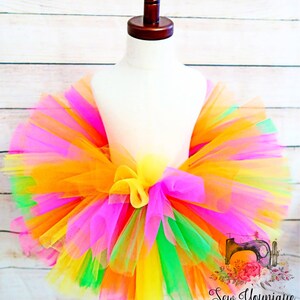Puede incluir: Una falda de tut&uacute; de tul de colores con capas de tul naranja, amarillo, rosa, verde y verde lima. La falda est&aacute; atada con un lazo en la cintura.