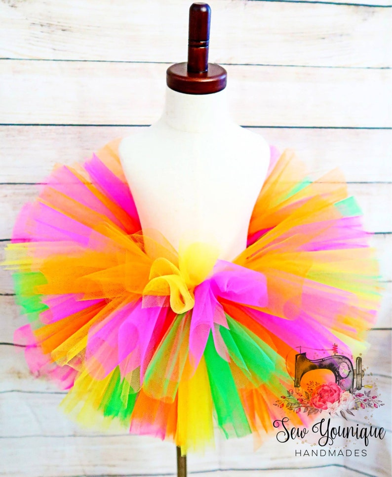 Puede incluir: Una falda de tut&uacute; de tul de colores con capas de tul naranja, amarillo, rosa, verde y verde lima. La falda est&aacute; atada con un lazo en la cintura.