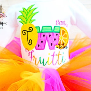 Puede incluir: Un body blanco con un dise&ntilde;o bordado de colores de una pi&ntilde;a, una sand&iacute;a y una naranja. El body dice "Eastin Two Frutti" en una fuente de colores. El body se combina con un tut&uacute; de tul multicolor.