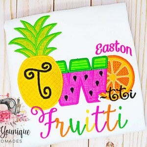 Puede incluir: Una camiseta blanca con un dise&ntilde;o bordado de colores que incluye una pi&ntilde;a, una sand&iacute;a y una naranja. El dise&ntilde;o dice "Two Fruitti" y "Easton" en letras rosas.