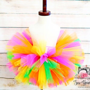 Puede incluir: Una falda de tut&uacute; de tul de colores con capas de tul rosa, amarillo, naranja y verde. La falda est&aacute; en un maniqu&iacute; blanco.