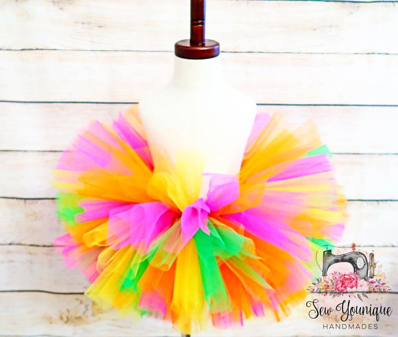 Puede incluir: Una falda de tut&uacute; de tul de colores con capas de tul rosa, amarillo, naranja y verde. La falda est&aacute; en un maniqu&iacute; blanco.