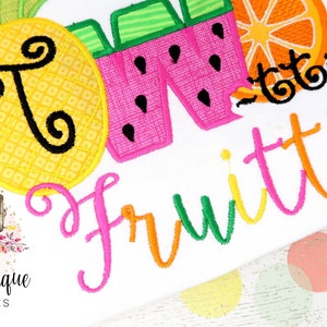 Puede incluir: Una camisa blanca con dise&ntilde;os de frutas bordadas de colores. La camisa dice "So Fruitti" en una fuente de letra cursiva de colores.