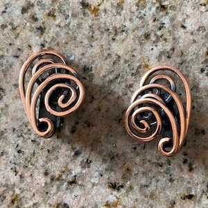 May include: A pair of copper-colored earrings with a swirling, organic design. The earrings are made of wire and have a delicate, feminine look.