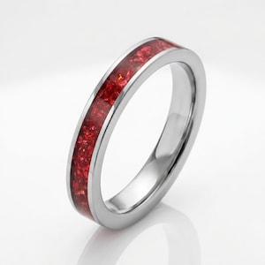 May include: A silver-toned metal ring featuring a smooth, polished band with a central inlay of crushed, deep red material. The ring has a rounded profile and a reflective surface, showcasing a consistent band width throughout its circular design.