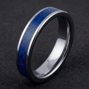 Op de afbeelding: Een zilveren ring met een levendige blauwe steen inleg. De ring heeft een gepolijst, reflecterend oppervlak en een band van diepblauw, getextureerd materiaal. Het ontwerp is eenvoudig maar elegant, geschikt voor dagelijks gebruik.