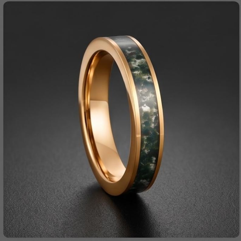 May include: A polished rose gold-toned ring featuring a central inlay of dark green and white mottled stone. The band has a smooth, reflective metallic finish on the edges, framing the textured, organic appearance of the stone inlay.