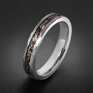 May include: A silver-toned metal ring featuring a faceted, hammered exterior surface and a central inlay of dark, textured material with visible brown and black inclusions running horizontally around the entire circumference of the band.