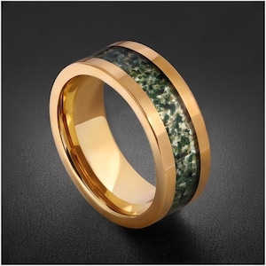 May include: A gold-toned band ring featuring a polished metallic finish and a central inlay of mottled green and white stone. The ring has a smooth, rounded interior and beveled edges, showcasing a distinct contrast between the shiny metal and the textured, organic appearance of the stone inlay.