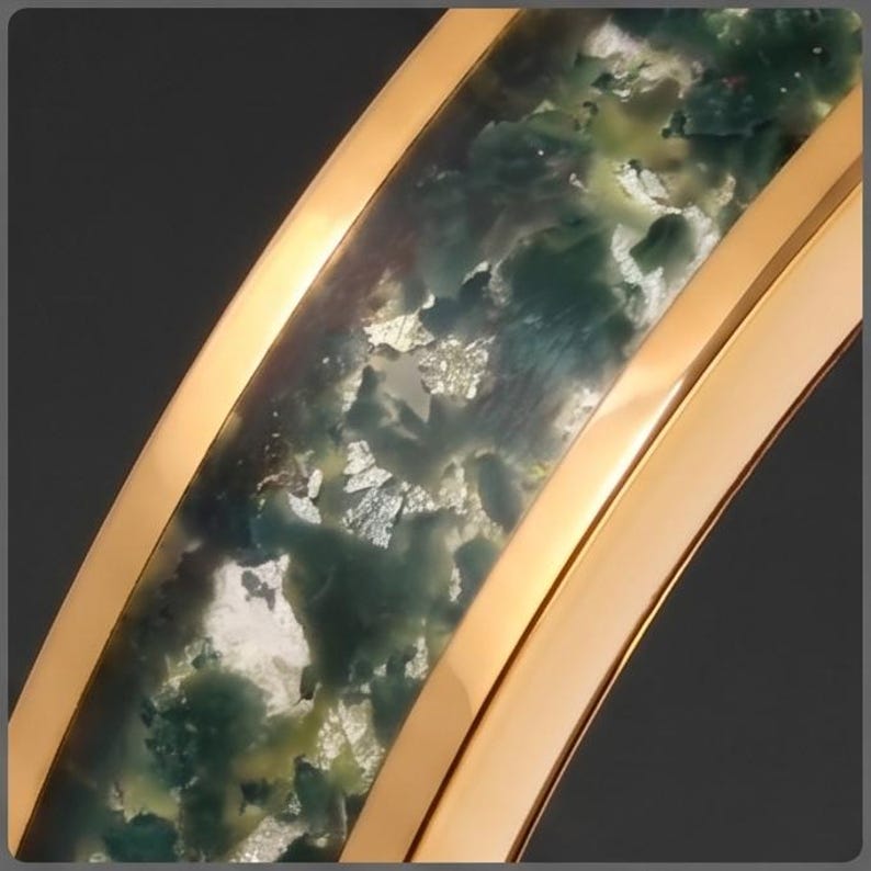 May include: A curved gold-toned ring featuring a central inlay of translucent resin with swirling dark green, teal, and mossy patterns interspersed with reflective silver-colored metallic flakes throughout the entire length of the band.
