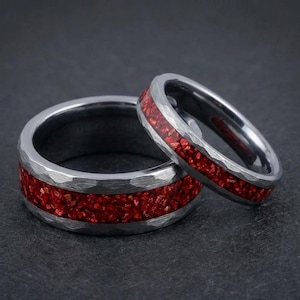 Peut inclure: Deux bagues en argent avec une texture martelée et une incrustation rouge vif. Les bagues sont probablement des alliances ou des accessoires de mode, présentant un design moderne avec un contraste de couleurs audacieux. Les bagues sont présentées sur une surface sombre.