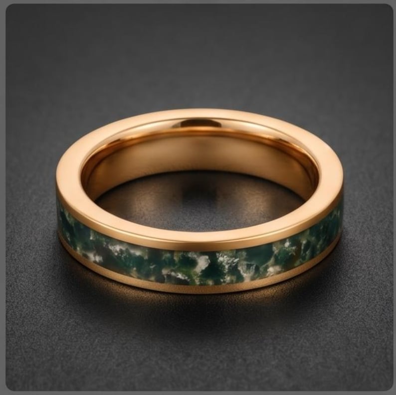 May include: A rose gold-toned band ring featuring a central inlay of dark green and white mottled stone. The ring has a smooth, polished metallic finish on the edges and a textured, organic appearance within the inlaid section of the band.