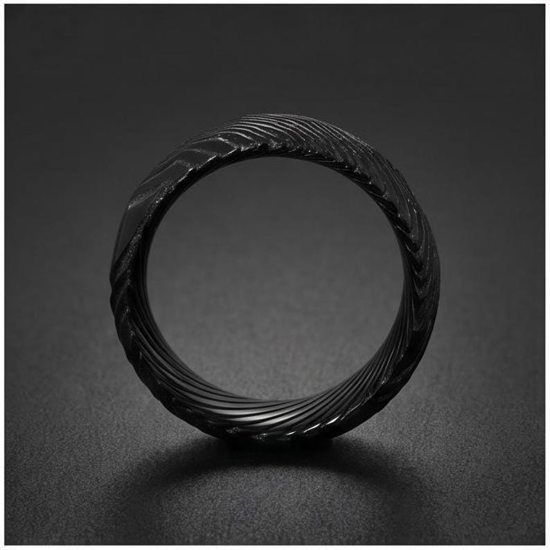 May include: A black ring featuring a textured surface with a repeating, diagonal, wave-like pattern that wraps around the entire band. The metal has a matte finish and a dark, monochromatic appearance, showcasing a consistent, intricate, and grooved design.