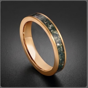May include: A rose gold-toned metal ring featuring a central inlay of moss agate stone. The band has a polished, smooth finish on the edges, while the inlay displays a mottled, dark green and translucent white pattern throughout the center.
