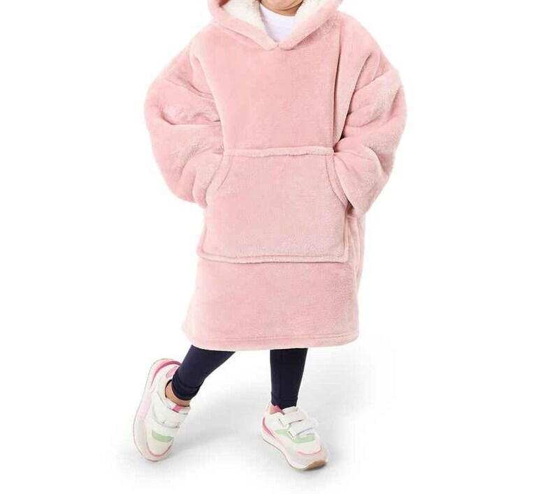 Puede incluir: Una manta de forro polar rosa con capucha y un gran bolsillo en la parte delantera. La manta la lleva puesta una persona y tiene un forro de polar blanco alrededor de la capucha.