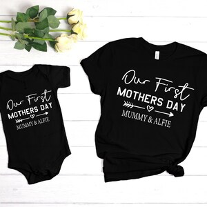 Może przedstawiać: Zestaw dopasowanych czarnych i białych koszulek i body z napisem "Our First Mothers Day" i strzałką z sercem. Pod strzałką znajduje się napis "Mummy & Alfie".