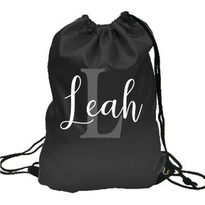 May include: Black drawstring bag with a white cursive name "Leah" and a large grey letter "L" in the centre.