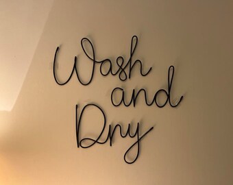 May include: Black metal wall decor with the words "Wash and Dry" in a cursive font.