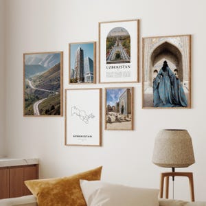 May include: A collection of framed art prints featuring images of Uzbekistan. The prints include a mountain road, cityscapes, architectural details, and a map of Uzbekistan. The prints are displayed on a white wall.