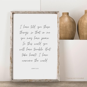 May include: A framed print with a white background and black text. The text is a quote from the Bible, John 16:33, which reads: "I have told you these things, so that in me you may have peace. In this world you will have trouble. But take heart! I have overcome the world."