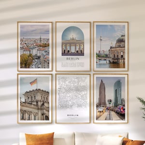 May include: Six framed prints with images of Berlin, Germany. The prints feature cityscapes, landmarks, and a map of the city. The prints are in wooden frames and are displayed on a white wall. The text "BERLIN" is visible on two of the prints.