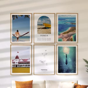 May include: Six framed art prints with wooden frames. The prints feature images of Tonga, including a woman on a hammock, a yellow boat on a beach, aerial views of the ocean, a building, a map, and a diver underwater.