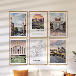 Puede incluir: Seis impresiones artísticas enmarcadas que representan lugares emblemáticos de Cincinnati, Ohio. Las impresiones incluyen paisajes urbanos, un puente, un mapa y detalles arquitectónicos. Los marcos son de color marrón claro y las impresiones se exhiben en una pared blanca.