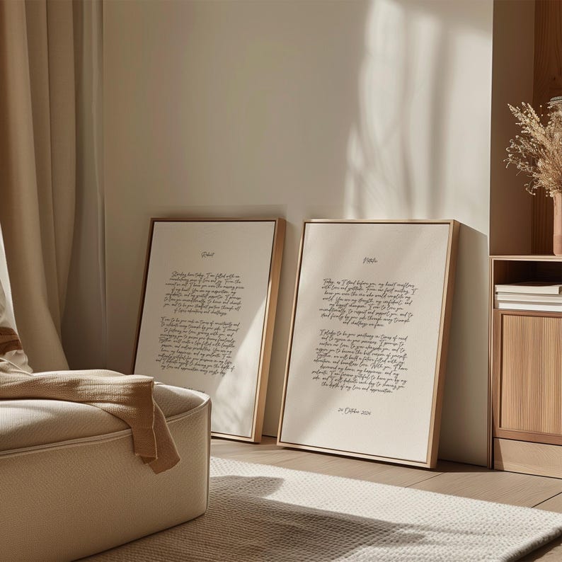 K&ouml;nnte beinhalten: Zwei gerahmte Drucke mit goldfarbenen Rahmen lehnen an einer Wand. Die Drucke zeigen handgeschriebenen Text in schwarzer Tinte auf cremefarbenem Hintergrund. Der Raum hat eine neutrale Farbpalette mit einem beigen Teppich und einer cremefarbenen Ottomane.