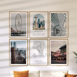May include: Six framed art prints featuring Seattle landmarks. The images include the Seattle Great Wheel, the Space Needle, a modern building, a city street view, a map of Seattle, and Pike Place Market. The prints are in wooden frames.