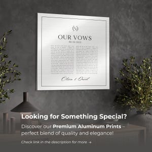 May include: A silver metal print with the text "OUR VOWS" and the date "06/24/2022". The print also includes the names "Olivia & David" and a floral design. The print is displayed on a table with a black lamp and green plants.