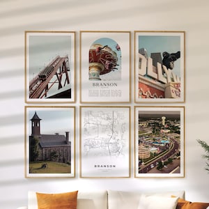 May include: Six framed prints featuring images of Branson, Missouri. The prints include a roller coaster, a Ferris wheel, a map, and other city landmarks. The prints are displayed on a white wall above a white couch with orange pillows.