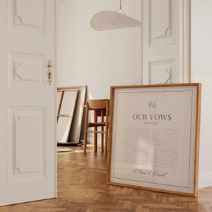 May include: A framed print with a light brown wooden frame. The print is white with black text that reads "Our Vows" and the date "06.24.2022". The text "Olivia & David" is at the bottom of the print.