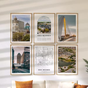 May include: Six framed art prints featuring images of Des Moines, Iowa. The prints include cityscapes, a bridge, and a map. The frames are a light brown color, and the prints are displayed on a white wall.