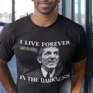 Könnte beinhalten: Ein schwarzes T-Shirt mit einem grafischen Aufdruck eines Mannes mit Zähnen und dem Text "Ich lebe für immer in der Dunkelheit".