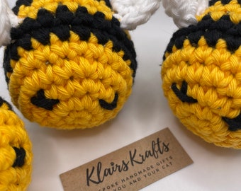 May include: Three crocheted bee toys with black and yellow stripes and white wings. The toys are handmade and are on a brown card with the text "Klairs Krafts Bespoke Handmade Gifts For You and Your Cat".