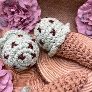 Op de afbeelding: Twee gehaakte ijshoorns, een groene met bruine chocolade chips en een bruine, op een houten oppervlak met roze bloemen.