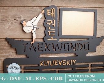 May include: Black metal medal display with the word "TAEKWONDO" in white lettering. The display has a cutout of a person doing a taekwondo kick. The display also has a rectangular space for a photo and a nameplate that reads "KLYUEVSKIY".