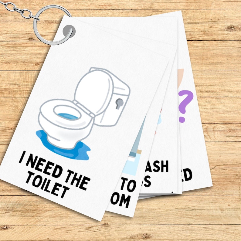 May include: A set of white cards with black text and illustrations. The cards have phrases like "I need the toilet" and "Wash hands". The cards are attached to a silver key ring.