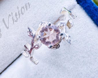 May include: A silver ring with a delicate floral design featuring a pink gemstone. The ring is displayed in a blue velvet box.