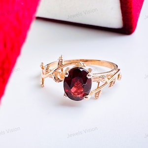 May include: A gold ring with a red gemstone and a delicate leaf design. The ring is set on a white background.