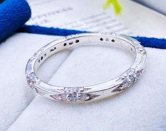 May include: A silver band ring with a row of small, clear stones set in a delicate design. The ring is in a white box with blue velvet lining.