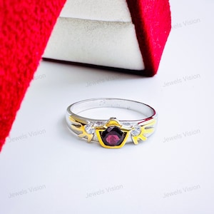 May include: A silver ring with a gold band and a red gemstone. The ring has two small white gemstones on either side of the red gemstone.