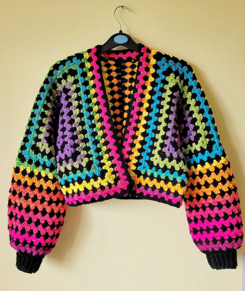 K&ouml;nnte beinhalten: Eine Regenbogen-H&auml;keljacke mit schwarzem Besatz und langen &Auml;rmeln. Die Jacke ist kurz geschnitten und hat einen V-Ausschnitt.