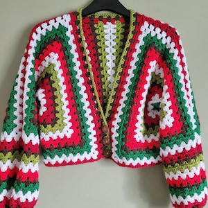 K&ouml;nnte beinhalten: Eine verk&uuml;rzte Strickjacke mit langen &Auml;rmeln, die ein farbenfrohes Streifenmuster in Rot-, Gr&uuml;n-, Wei&szlig;- und Braunt&ouml;nen aufweist. Die Strickjacke hat einen V-Ausschnitt und einen Knopfverschluss.