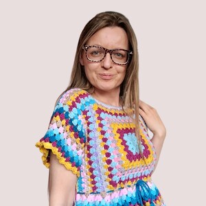 May include: A colorful crochet top with a square pattern in shades of pink, purple, yellow, and blue. The top has a ruffled hem and a tie at the waist.