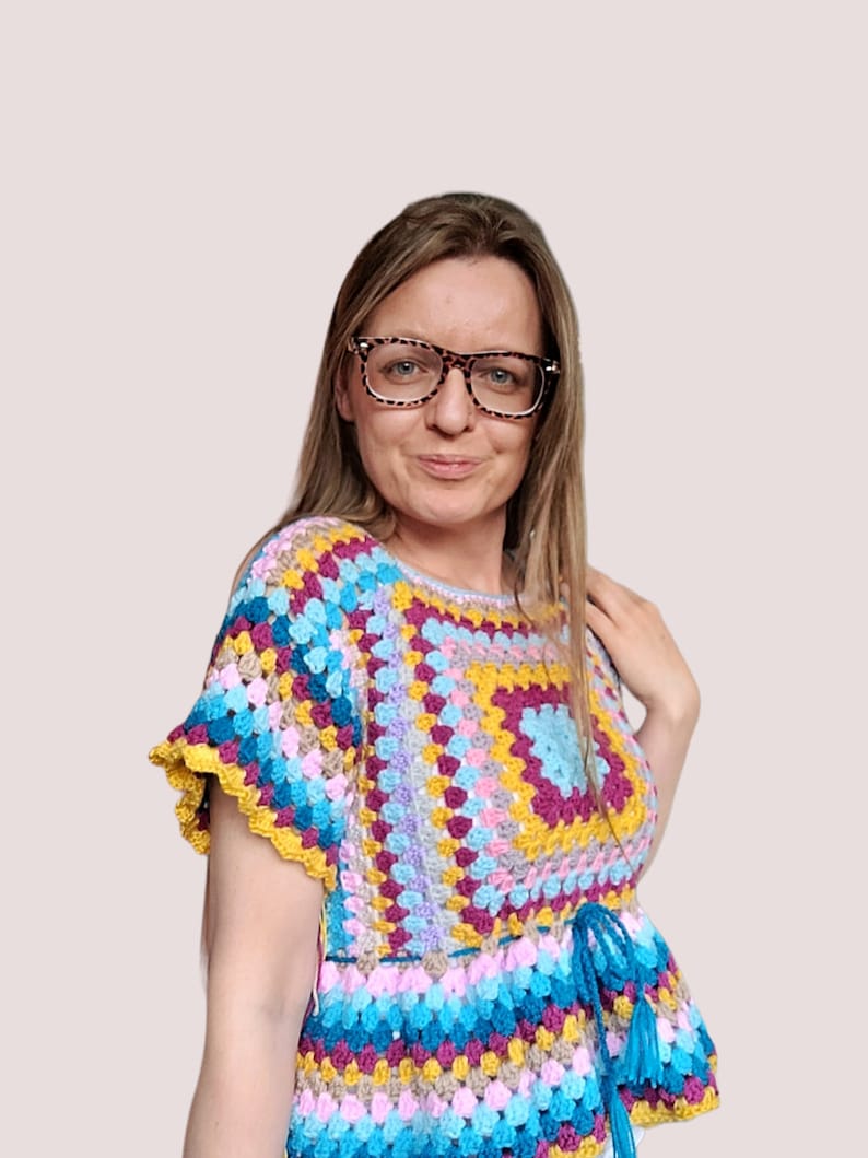 May include: A colorful crochet top with a square pattern in shades of pink, purple, yellow, and blue. The top has a ruffled hem and a tie at the waist.