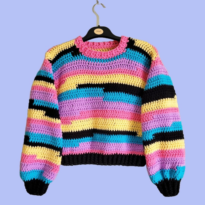 May include: A colorful striped crochet sweater with a crew neck and long sleeves. The sweater is made in a variety of colors, including pink, yellow, blue, and black.