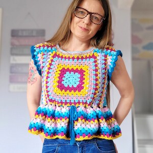 May include: A woman wearing a colorful crocheted top with a blue tie and blue jeans.