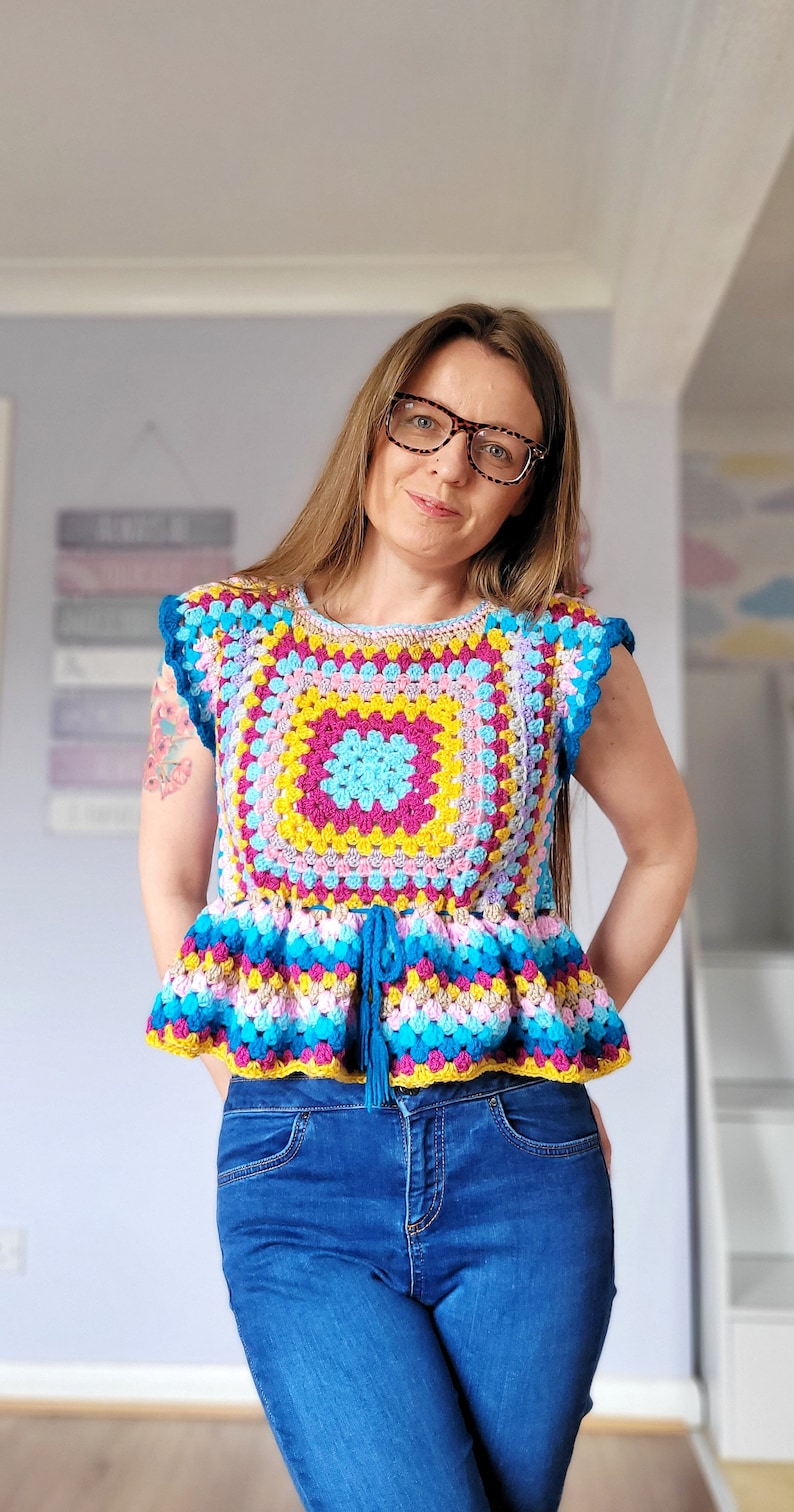 May include: A woman wearing a colorful crocheted top with a blue tie and blue jeans.